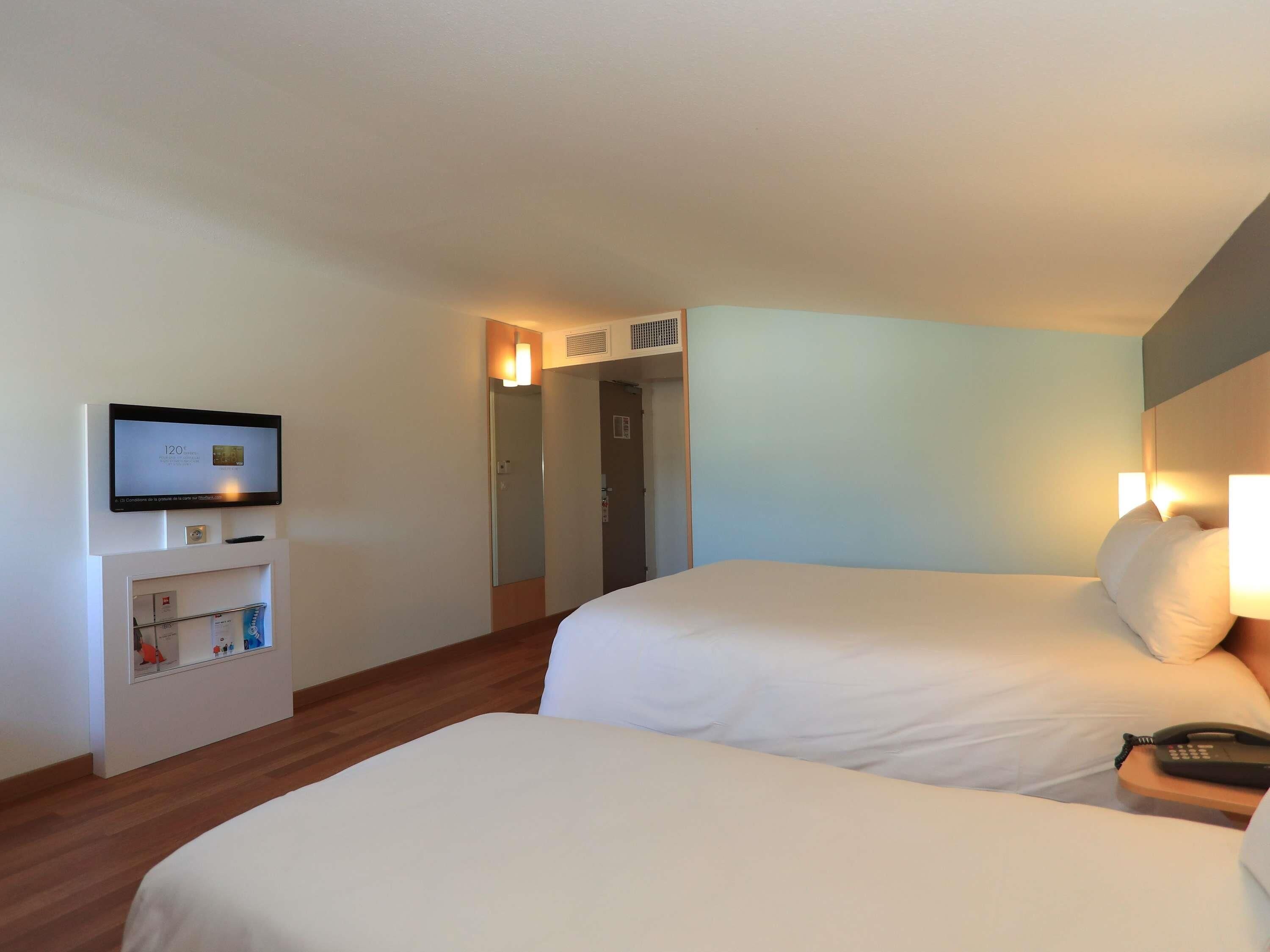 Une chambre d’hôtel avec deux lits, un téléviseur fixé au mur et une table de chevet avec un téléphone.