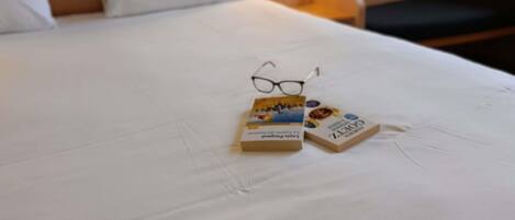 Una cama bien hecha con sábanas blancas, un par de gafas y dos libros sobre la cama.