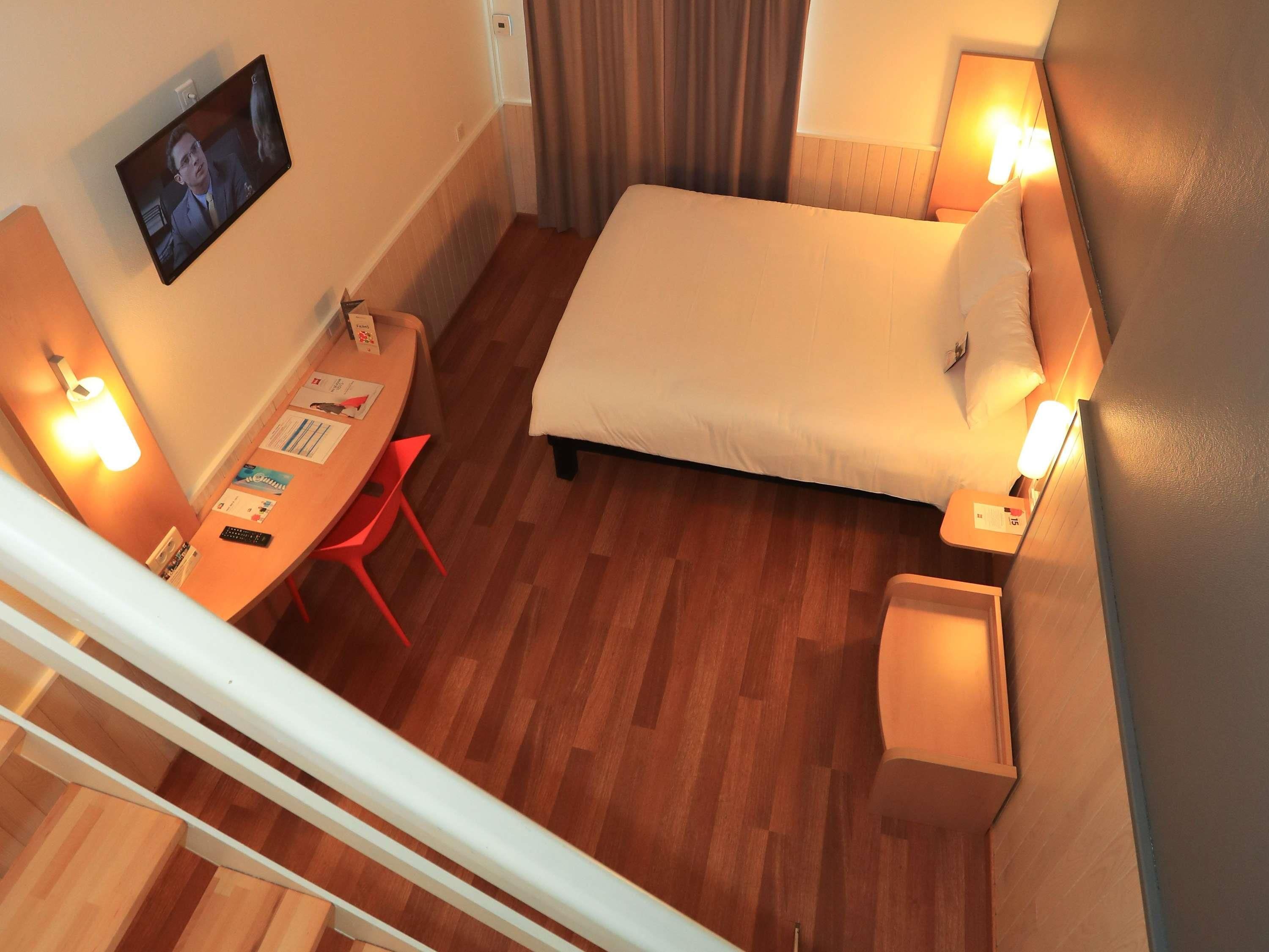 Une chambre d’hôtel comprenant un lit, un bureau avec une chaise, un téléviseur fixé au mur et deux lampes de chevet.