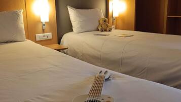 Habitación de hotel con dos camas, una mesita de noche, una lámpara, un oso de peluche y una guitarra.