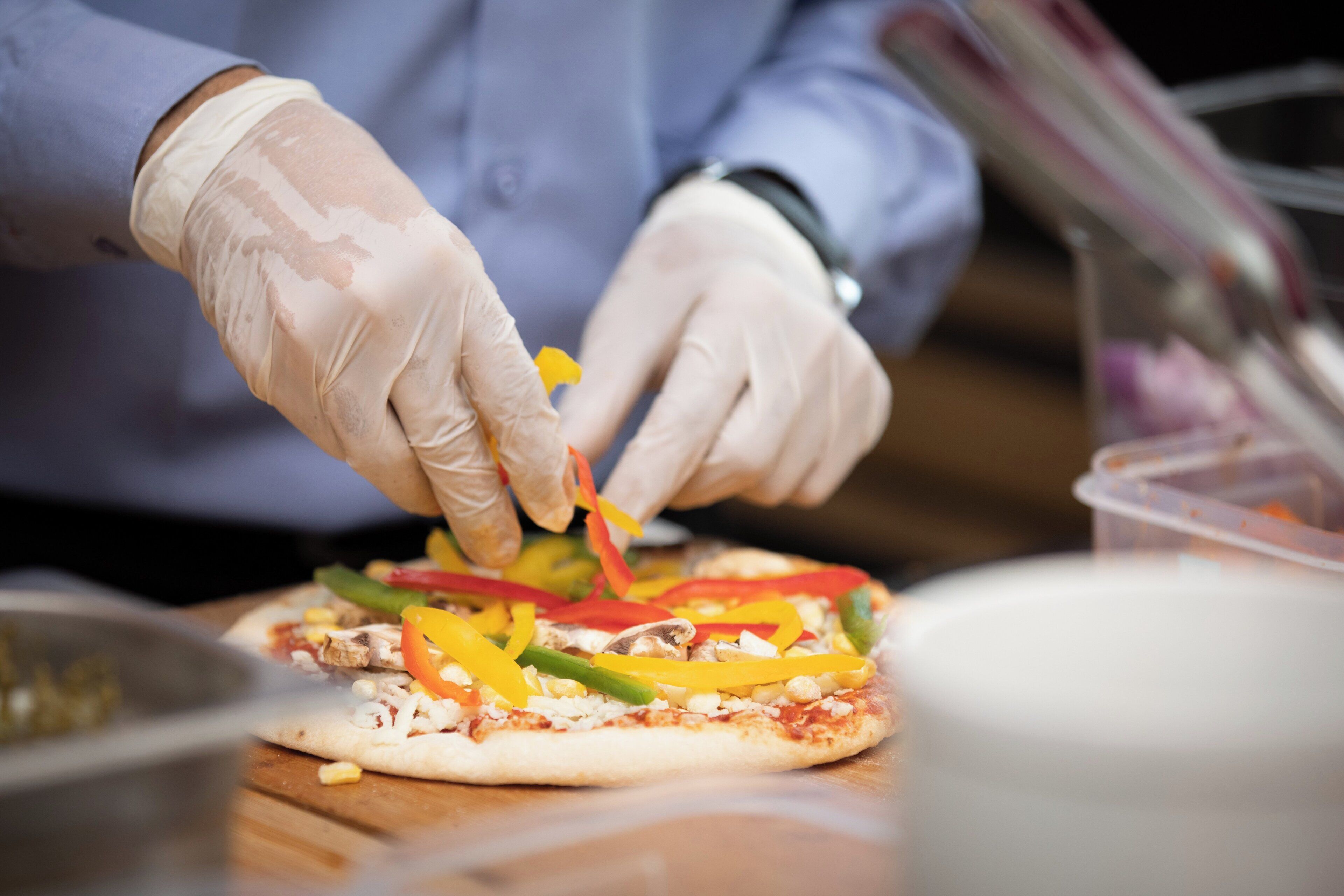 A person preparing food, specifically adding toppings to a flatbread.