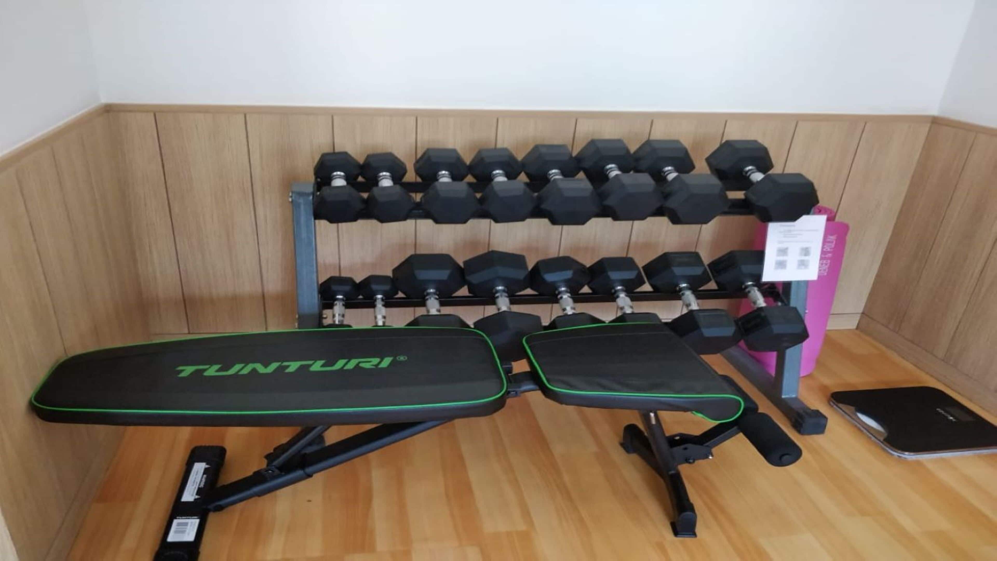 A weight bench with a Tunturi logo, a set of hexagonal dumbbells on a rack, and a smartphone on the floor.