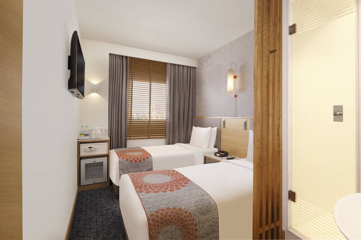 A hotel room with two beds, a desk, a minibar, and a shower area.