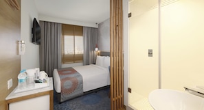 Una habitación de hotel con cama, escritorio con cafetera, televisor y baño con inodoro y lavamanos.
