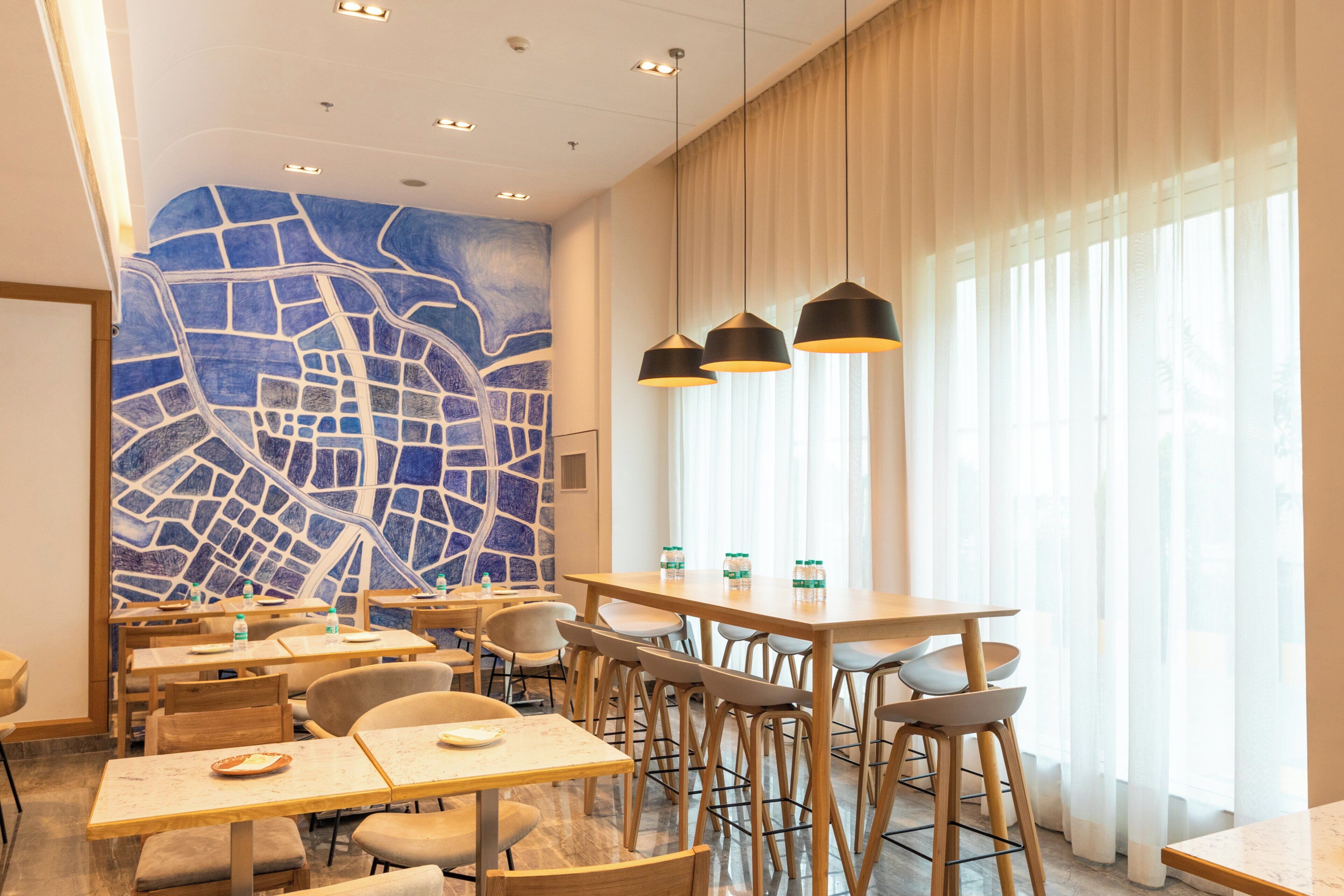 A hotel dining area with tables, chairs, and a cityscape mural on the wall.
