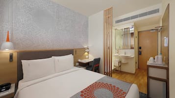 Een hotelkamer met een bed, nachtkastje, lamp en uitzicht op de badkamer.