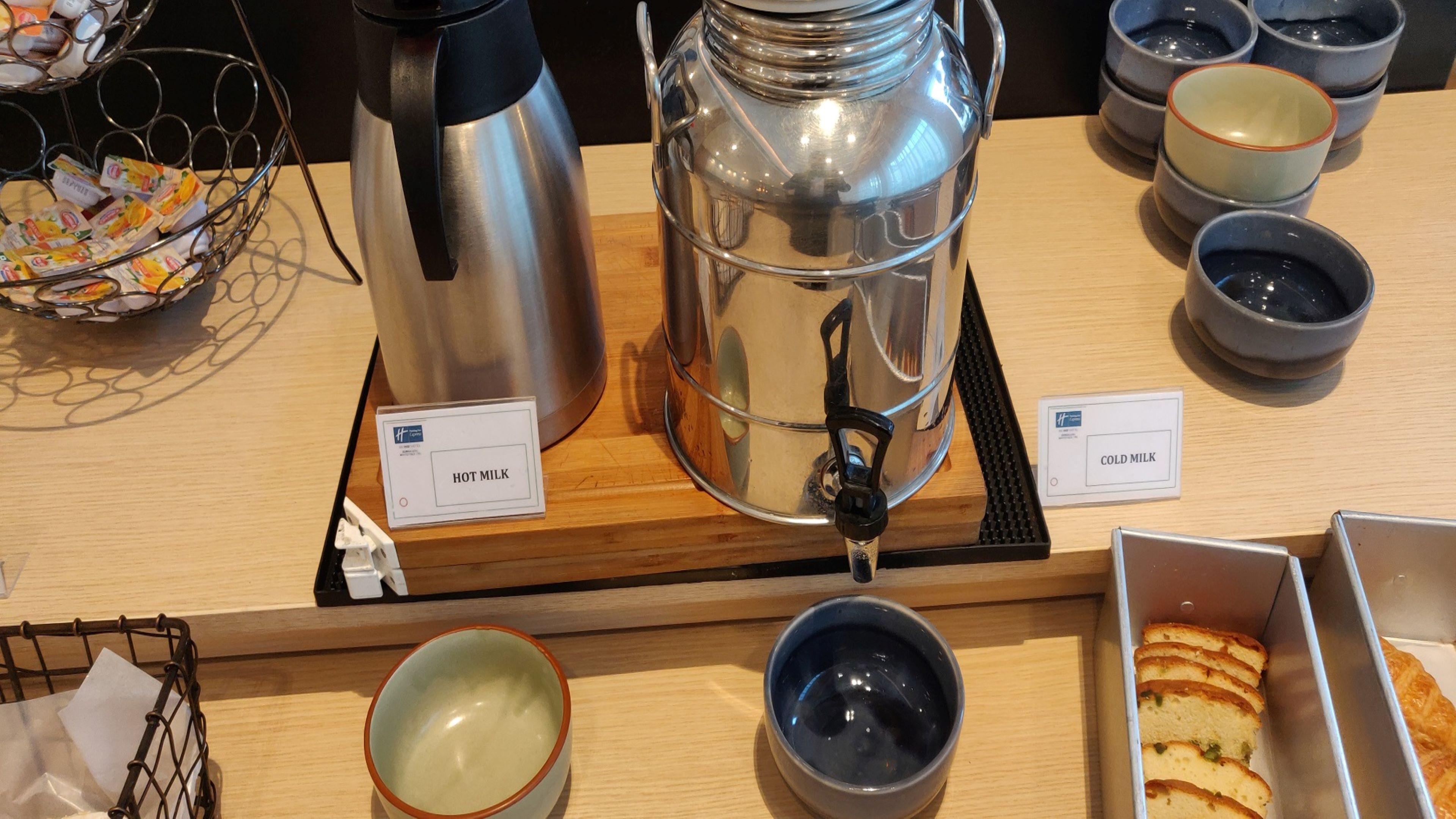A coffee station with a hot milk dispenser, a cold milk dispenser, and a tray of pastries.