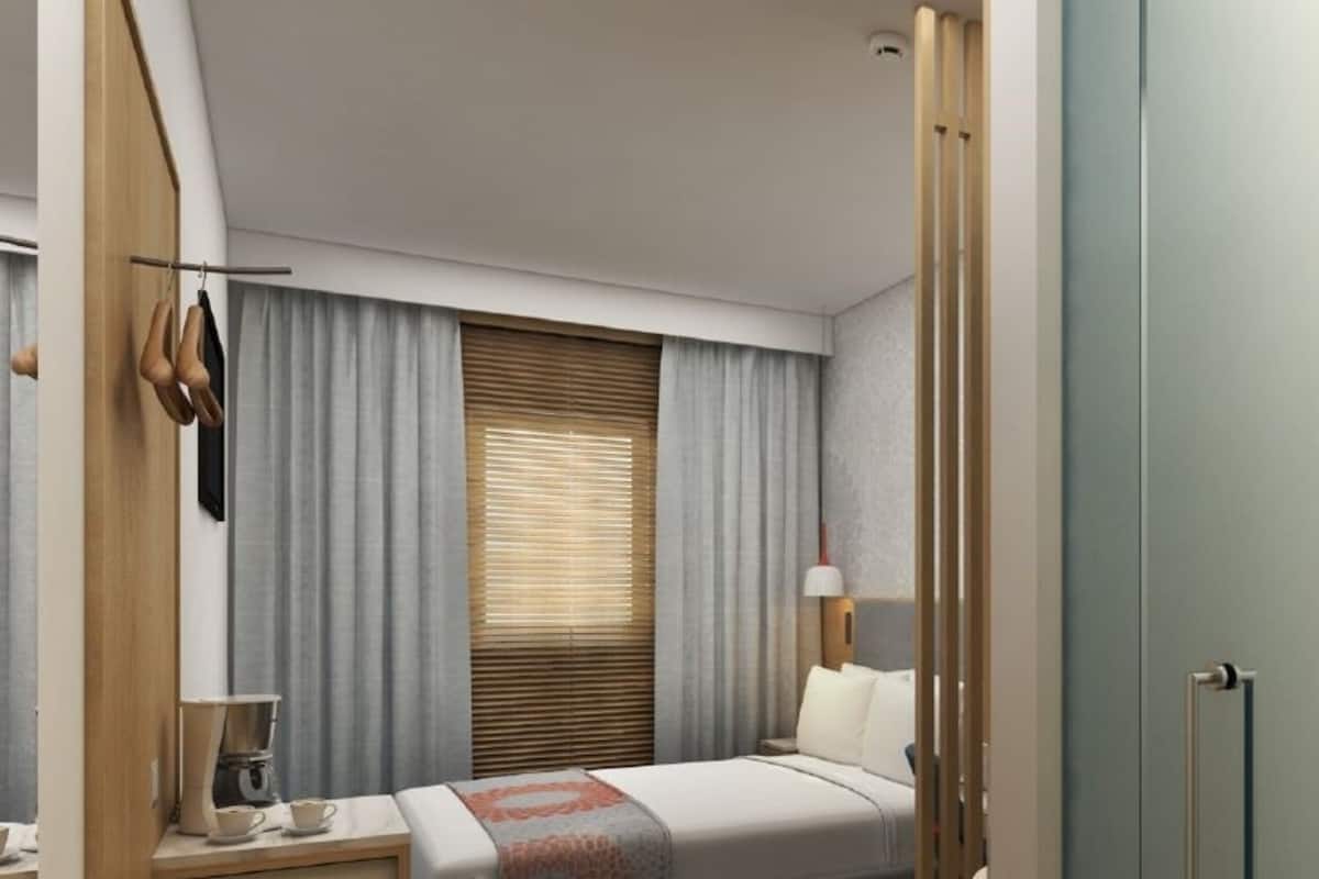 A modern hotel room with a bed, bedside table, lamp, and a view of the outside through the window.
