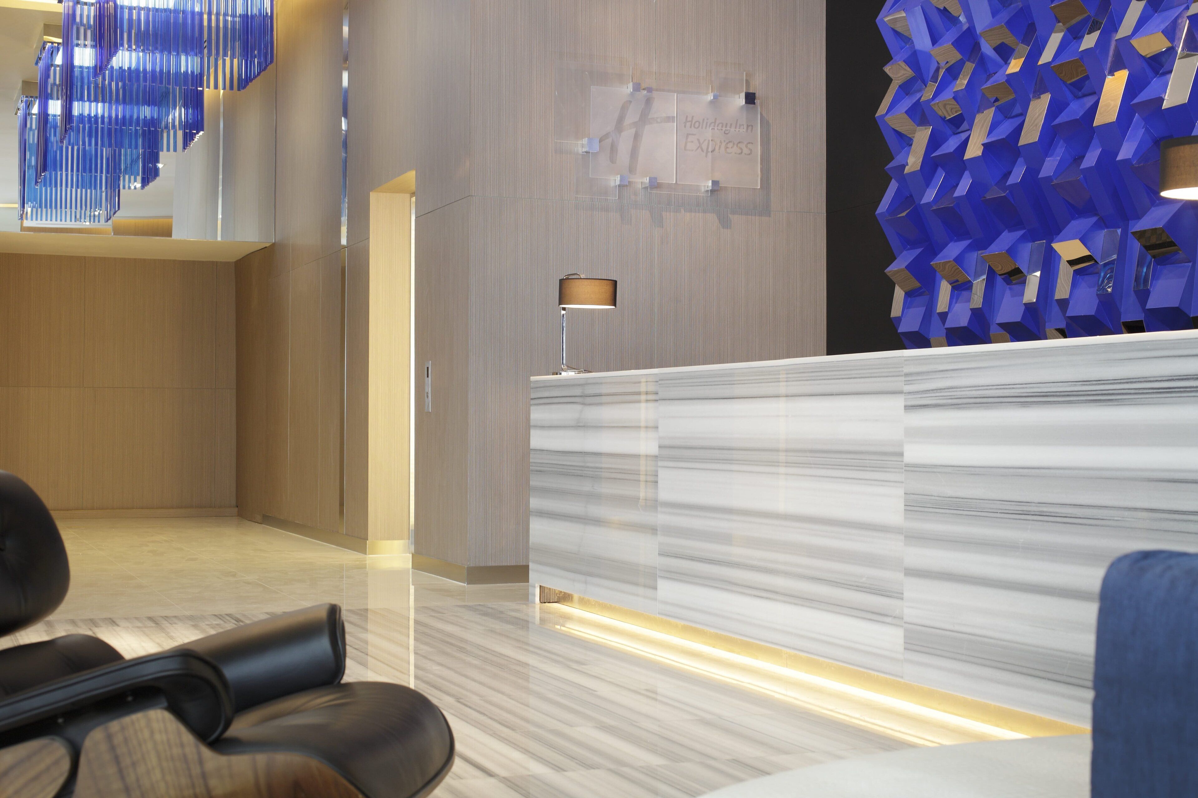 A modern reception area with a marble reception desk, a blue geometric wall feature, and a seating area with leather chairs.
