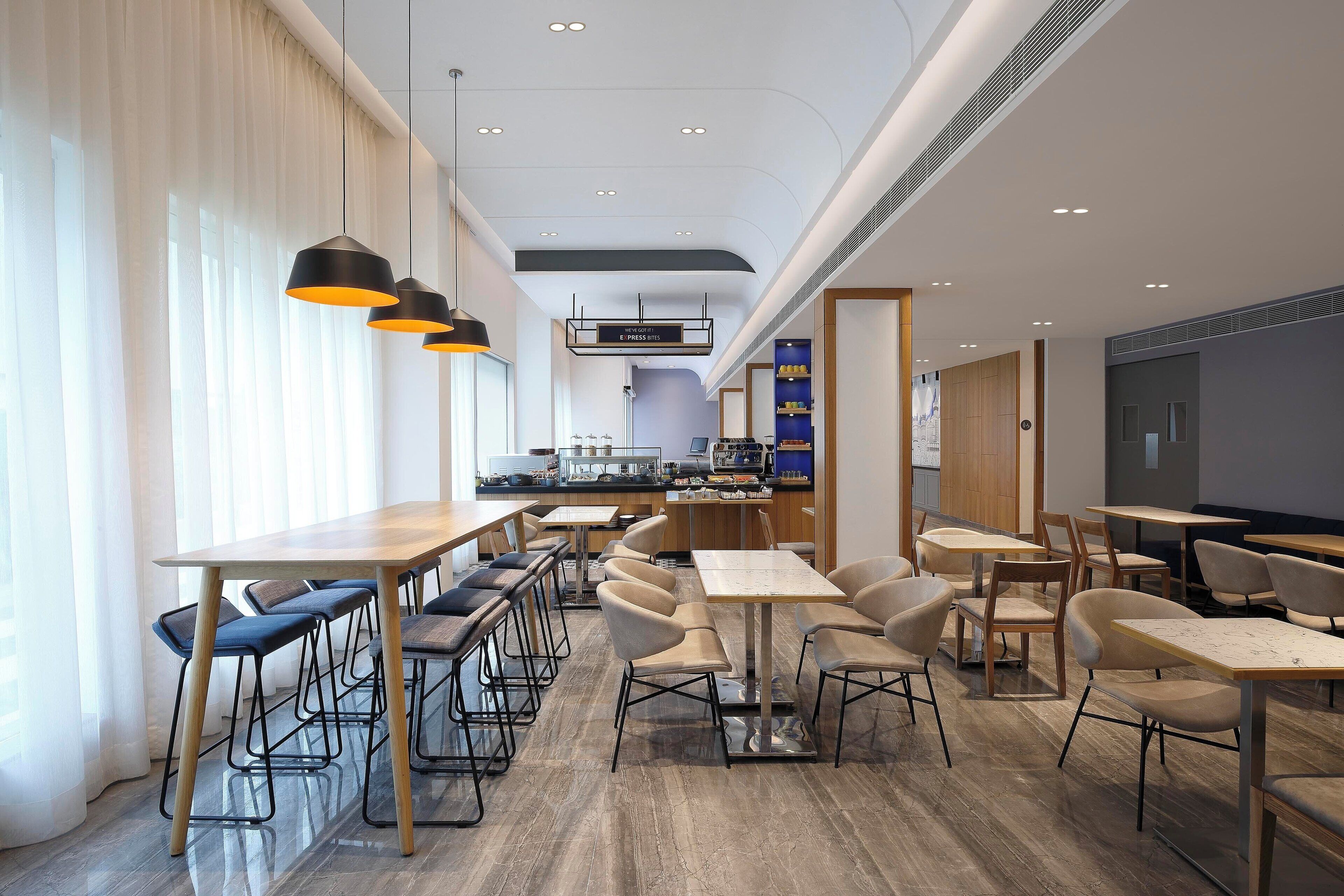 Ein modernes Café mit verschiedenen Sitzbereichen, darunter Tische und Stühle, und einer im Hintergrund sichtbaren Theke.