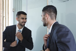Un hombre con traje se está arreglando la corbata frente a un espejo.