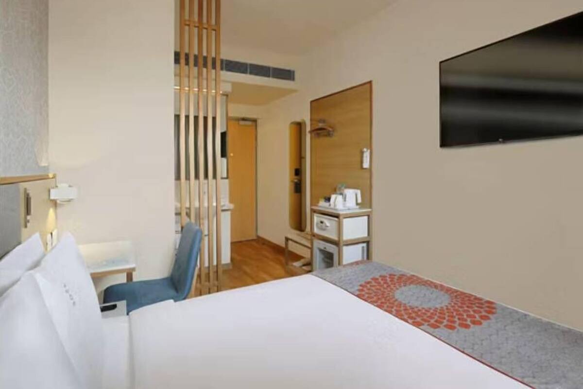 A hotel room with a bed, a desk, a chair, a mirror, and a television.