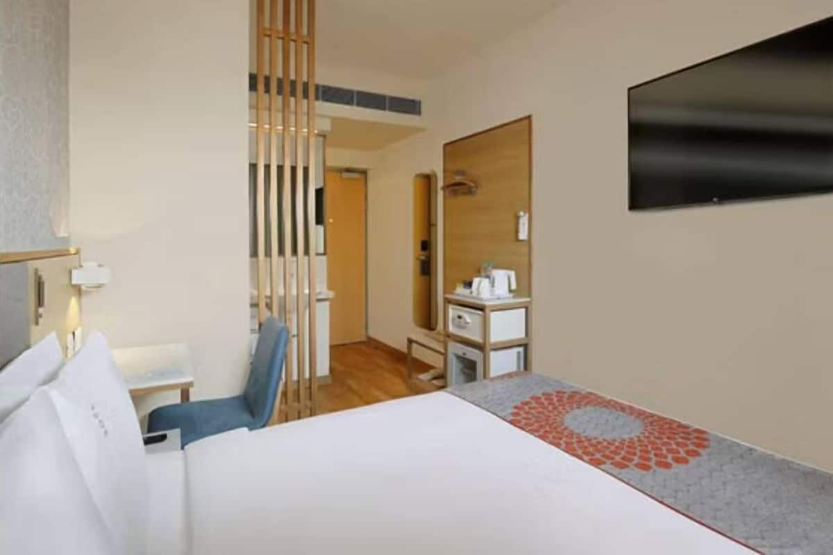 Une chambre d’hôtel équipée d’un lit, d’un bureau, d’une chaise, d’un miroir et d’une télévision.