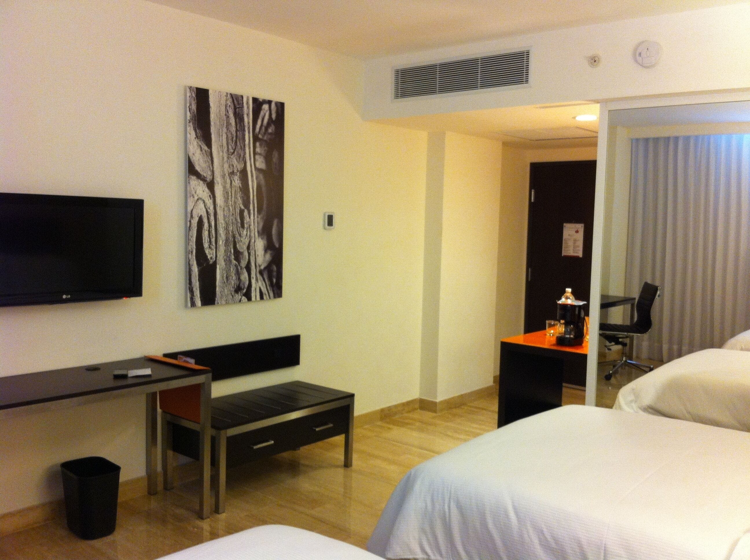 Habitación de hotel con cama, escritorio, silla, televisor y un cuadro en la pared.