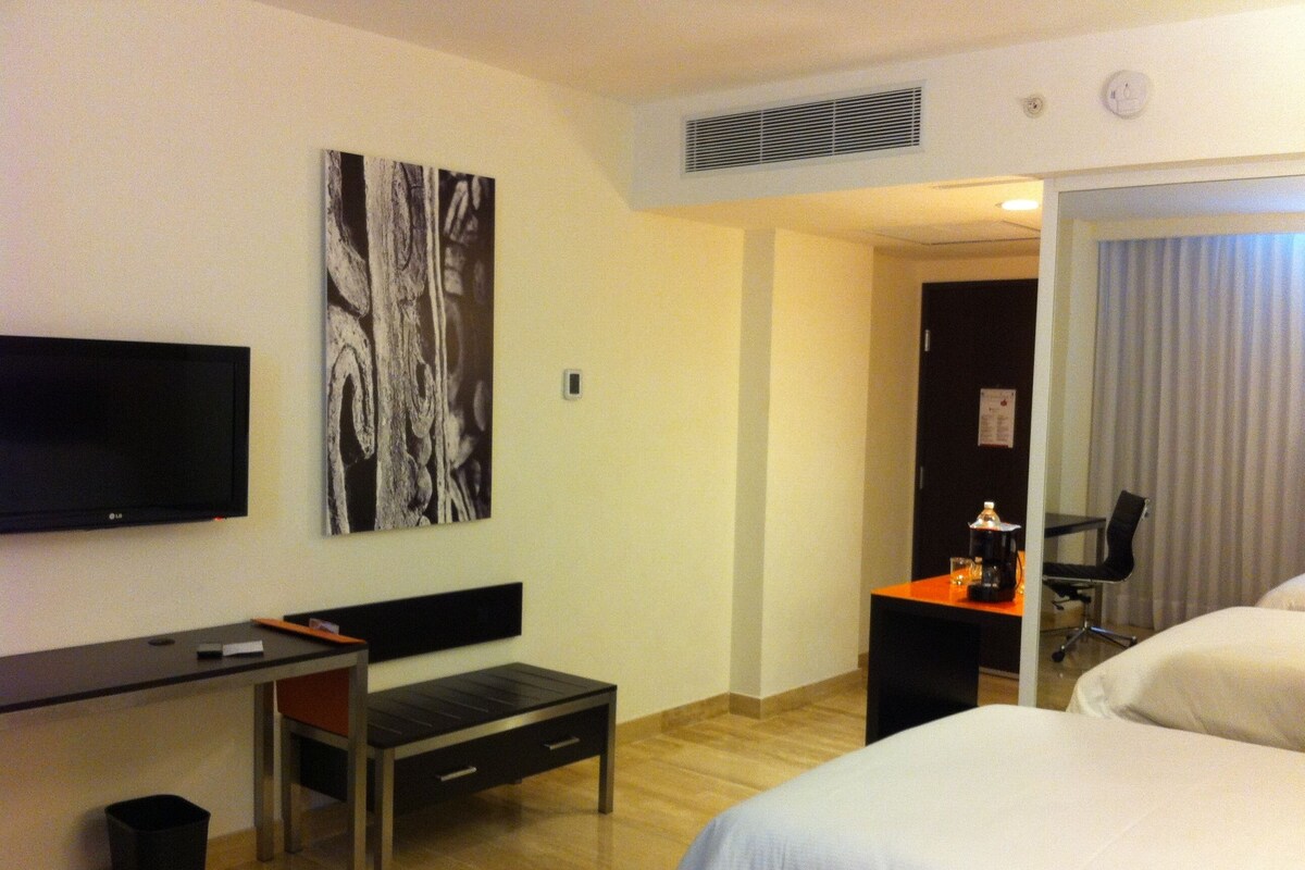 Een hotelkamer met een bed, een bureau, een stoel, een televisie en een schilderij aan de muur.