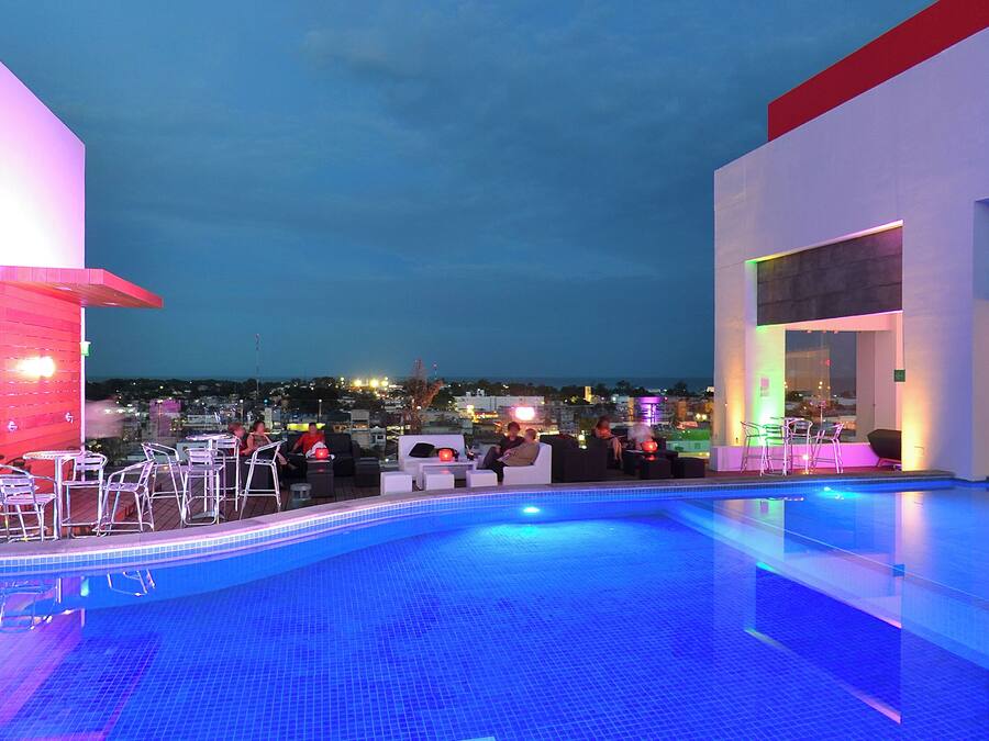 Zona de piscina en la azotea con sillones y mesas, rodeada de arquitectura moderna y vistas a la ciudad.