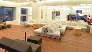 A modern living room with a sectional sofa, a round wooden coffee table, and a glass partition. - Fiesta Inn Chetumal Hotel (Chetumal)