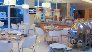 A modern dining area with white chairs, a buffet station, and a television mounted on the wall. - Fiesta Inn Chetumal Hotel (Chetumal)