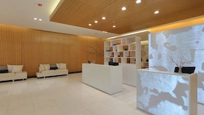A modern reception area with a wooden ceiling, white reception desk, and a seating area with sofas. - Fiesta Inn Chetumal Hotel (Chetumal)