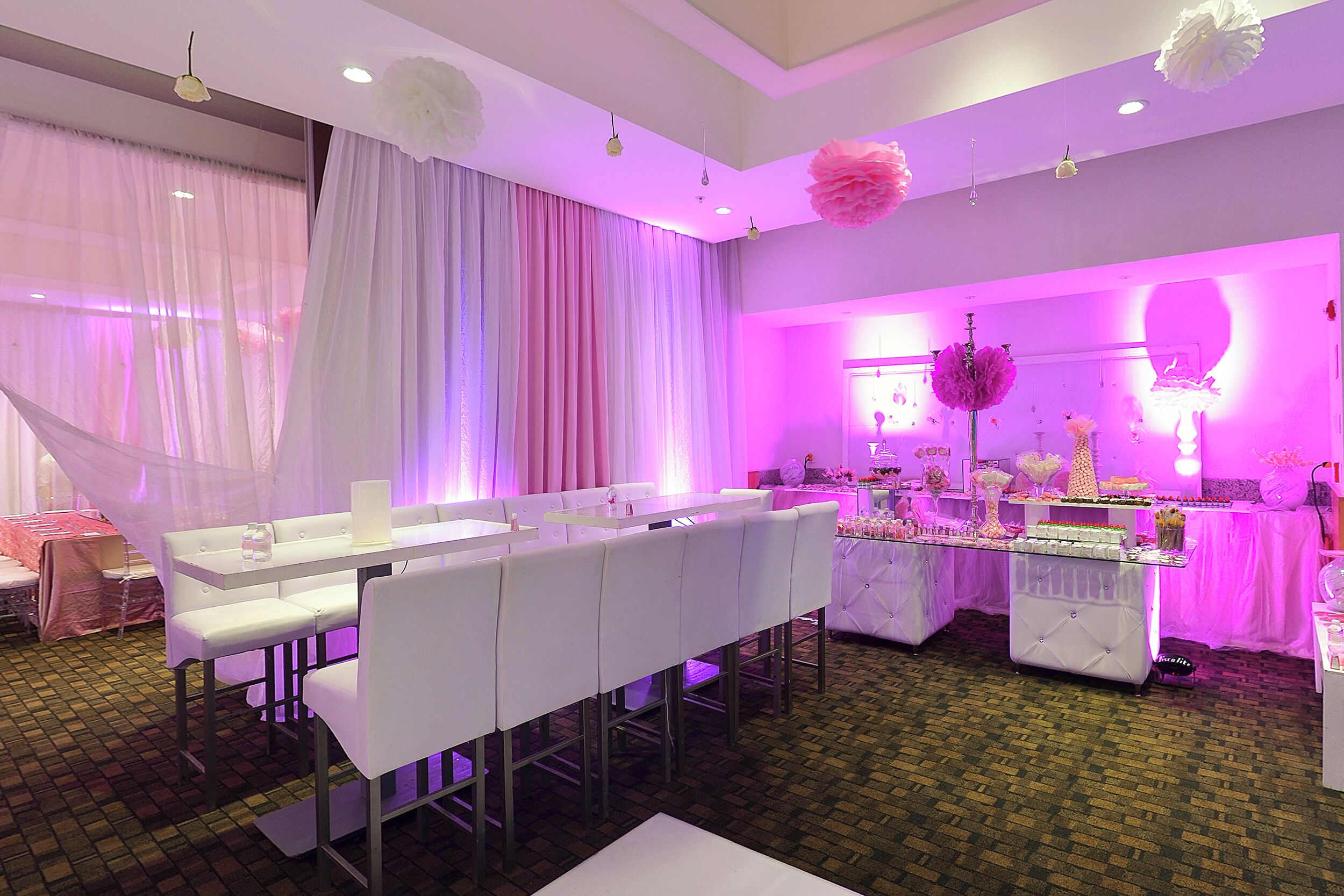 A banquet hall with white tables and chairs, a dessert display, and a floral arrangement.