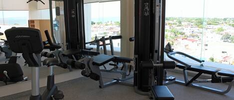 A gym with various exercise equipment, large windows, and a view of a cityscape.