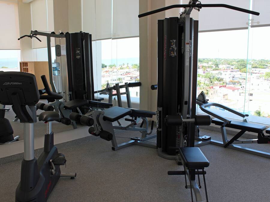 A gym with various exercise equipment, large windows, and a view of a cityscape.