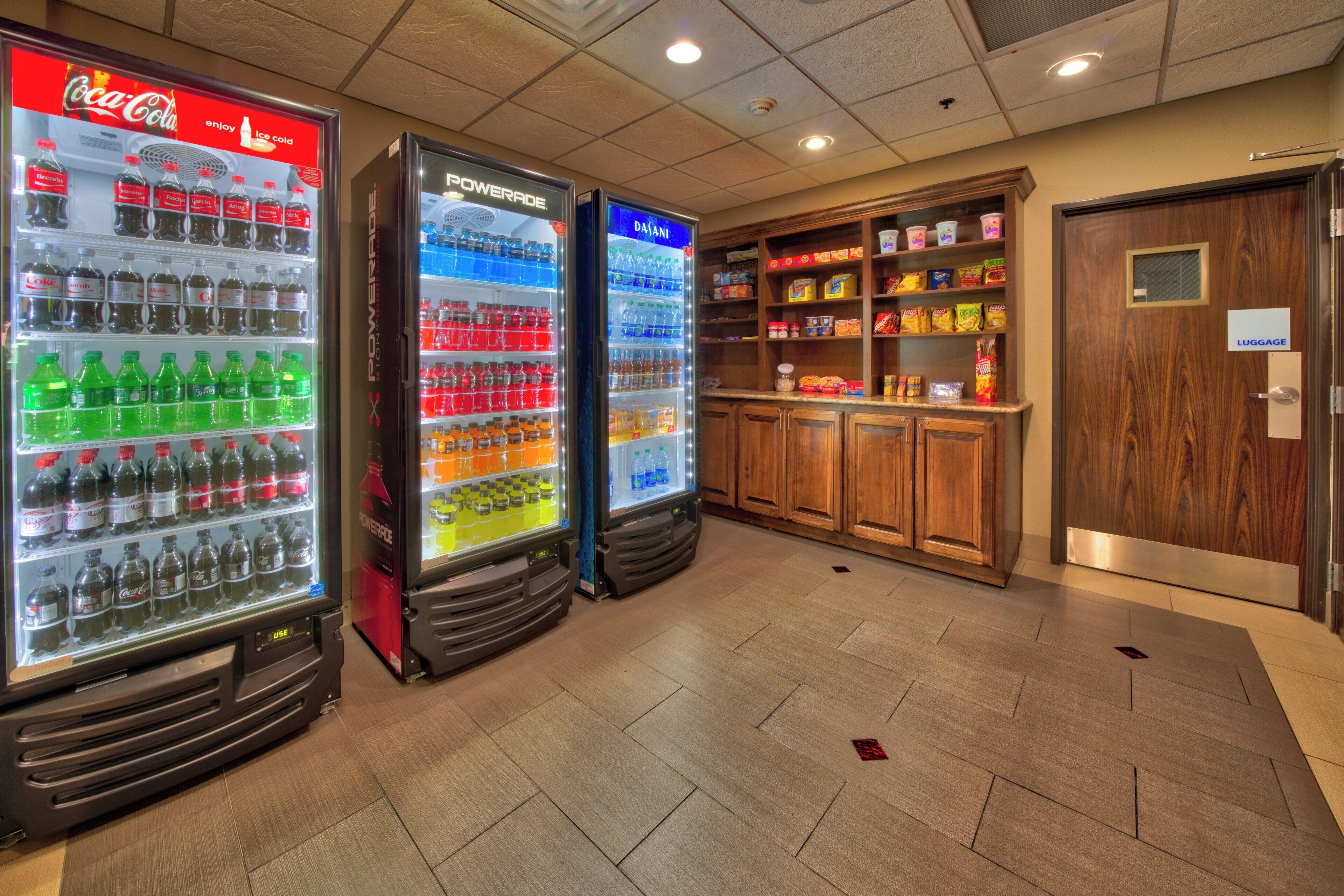 A hotel lobby with vending machines selling beverages, snack shelves, and a luggage storage area.