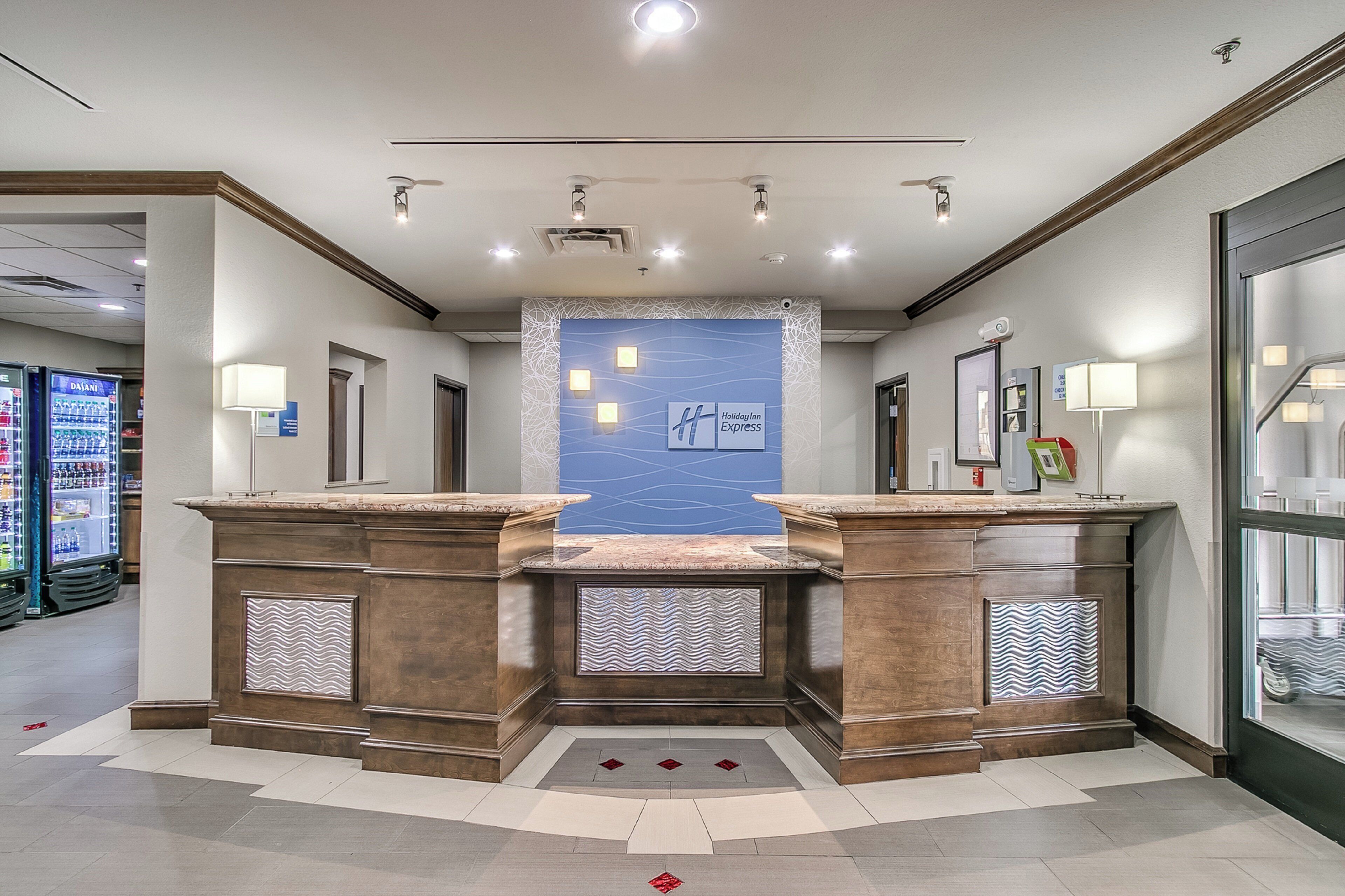 A hotel lobby with a reception desk, a blue accent wall, and a glass door leading to a parking area.