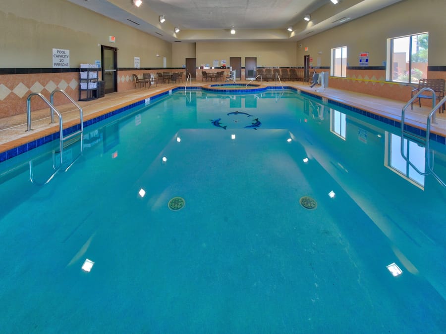 A large indoor pool with a capacity sign, lounge chairs, and a lifeguard chair.