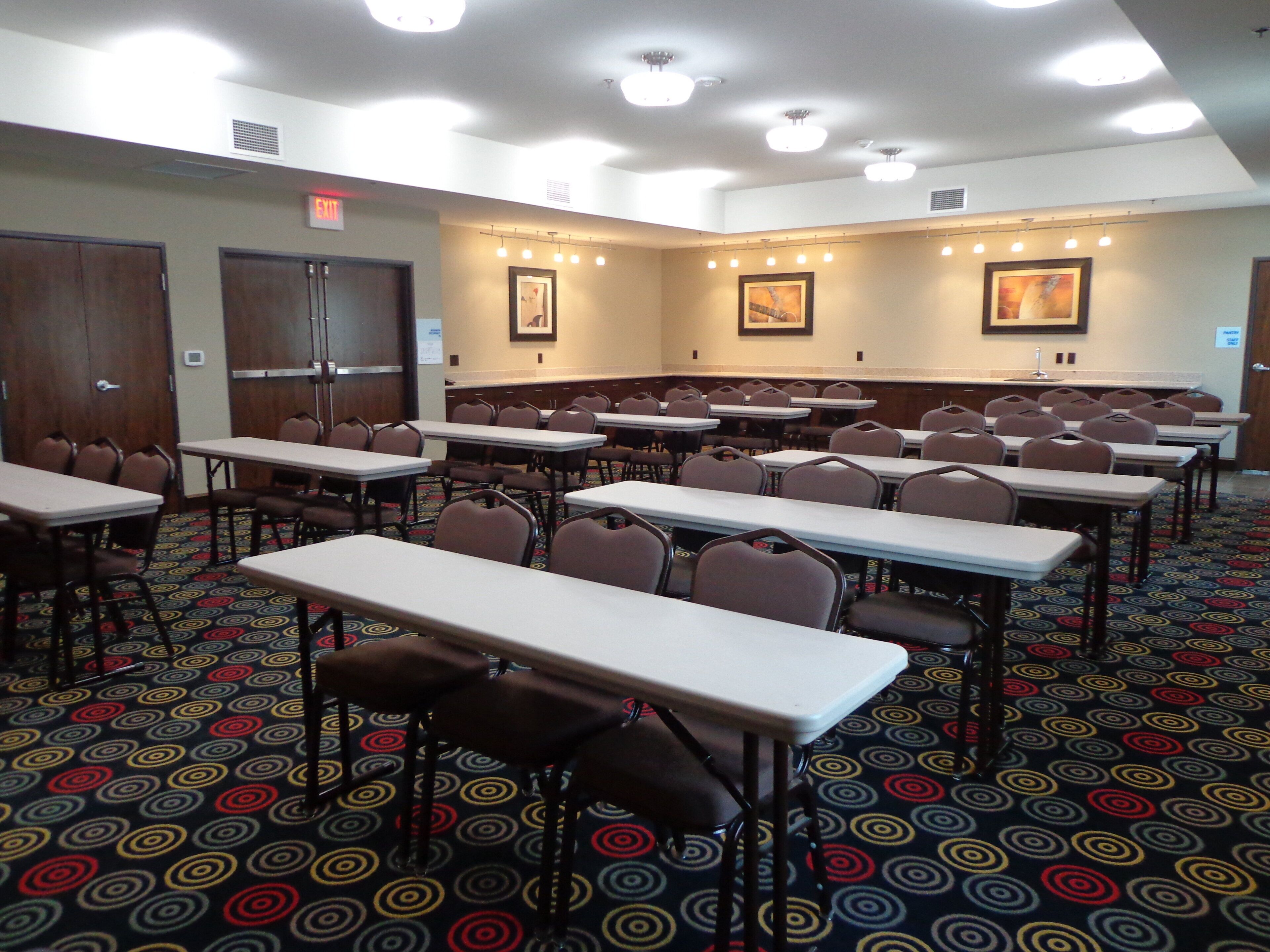 Une salle de conférence dotée de plusieurs tables et chaises, d’un tapis à motifs et d’œuvres d’art encadrées accrochées aux murs.