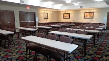 A conference room with multiple tables and chairs, a patterned carpet, and framed artwork on the walls.