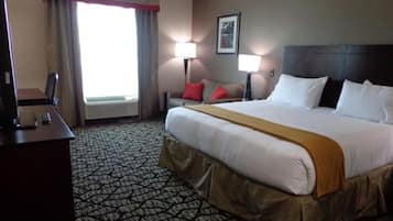 Une chambre d’hôtel avec un grand lit, un bureau avec un ordinateur, deux lampes de chevet et une fenêtre avec des rideaux.