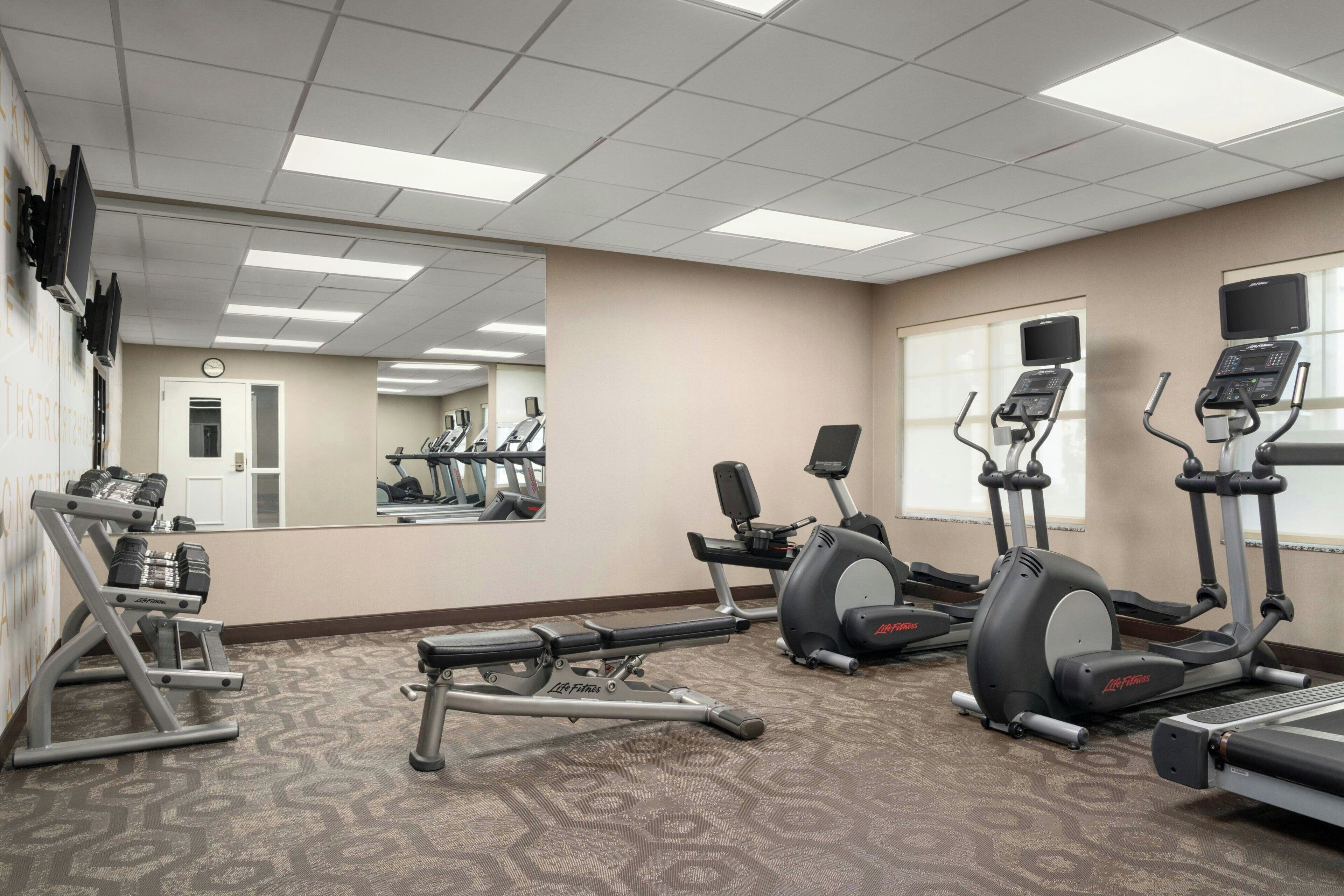 Uma academia com diversos equipamentos de exercício, um espelho grande e um relógio na parede.