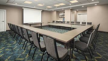 A conference room with a long table, chairs, a projector screen, and a carpeted floor.
