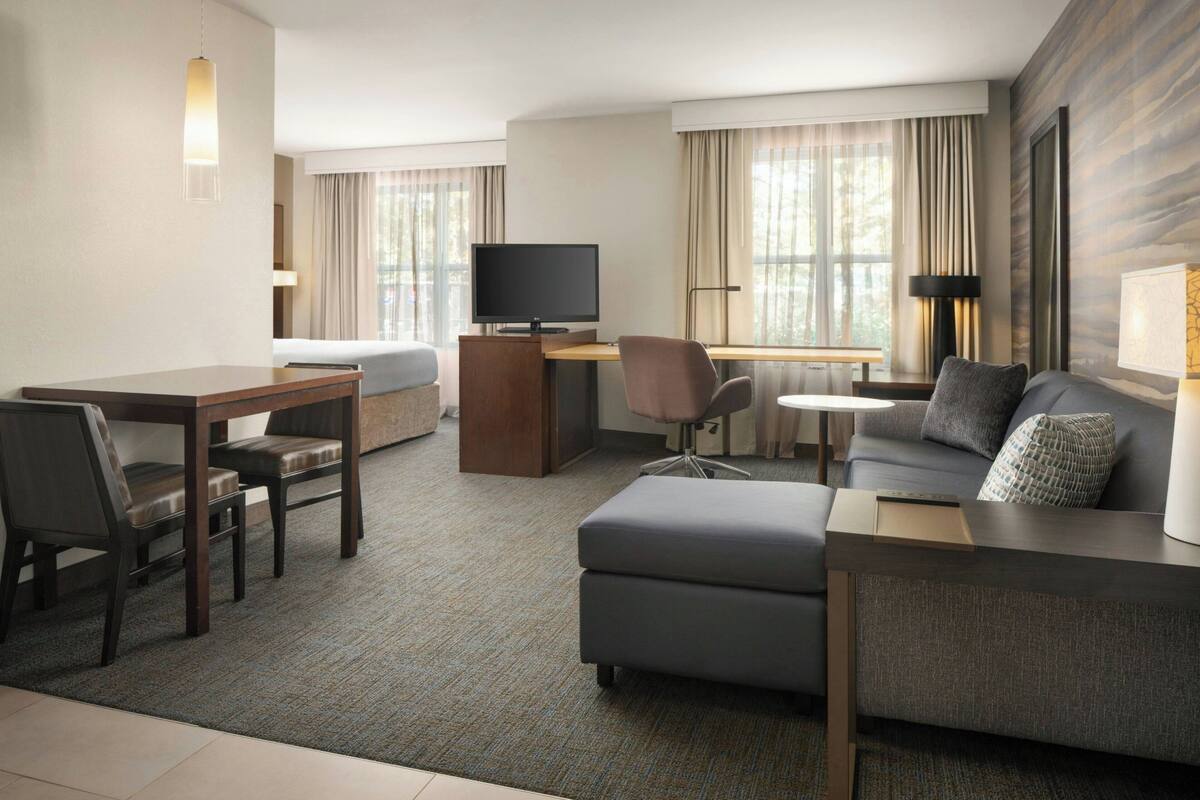 Habitación de hotel con sofá, escritorio con computadora, televisor y zona de comedor con sillas.