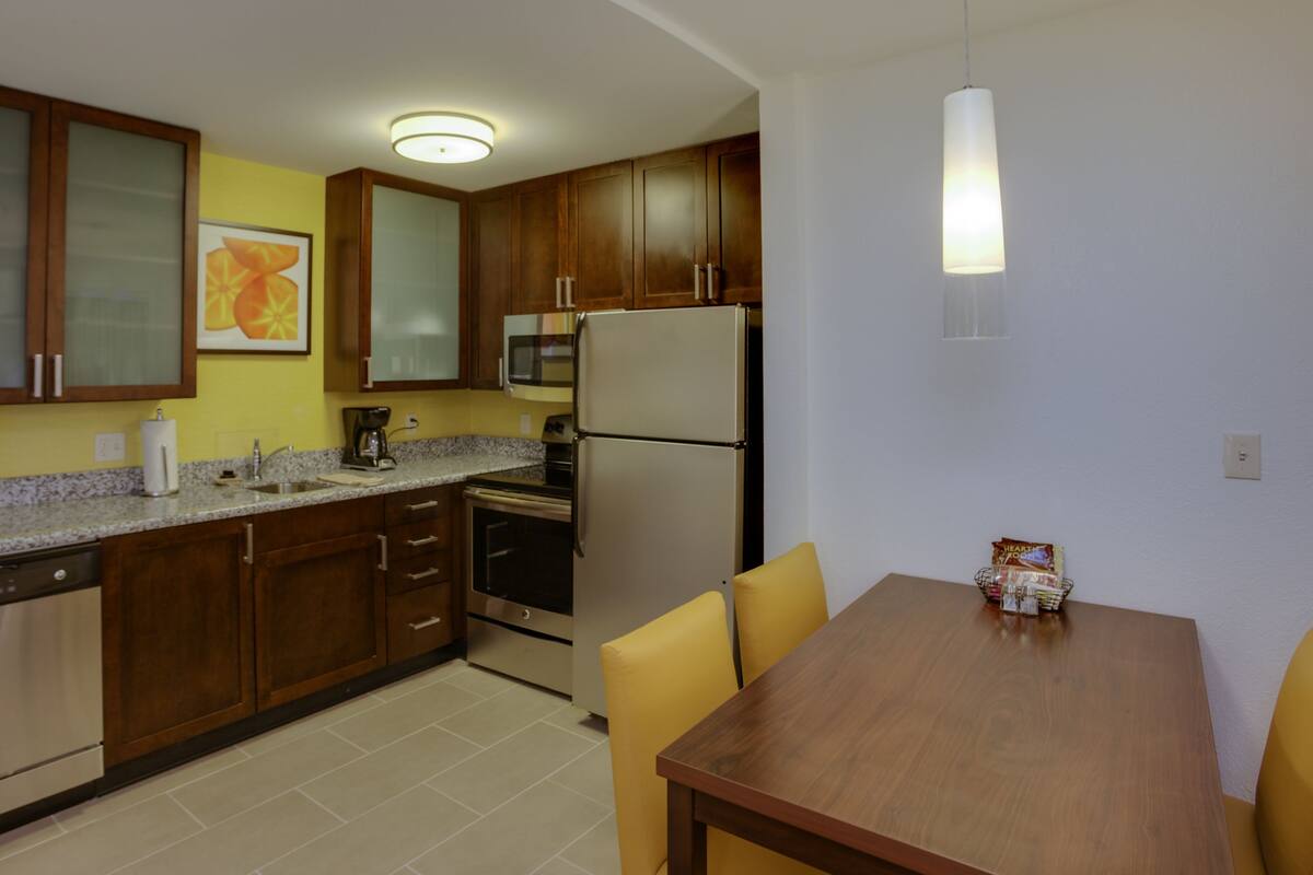 Una cocina compacta con armarios de madera, un refrigerador de acero inoxidable, un microondas y una mesa de comedor con sillas.
