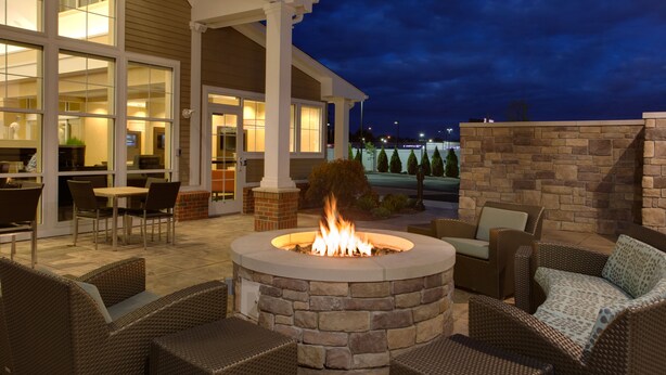 A patio area with a stone fire pit, wicker furniture, and a view of the building's interior. - Residence Inn Springfield Chicopee (Chicopee)