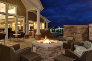 A patio area with a stone fire pit, wicker furniture, and a view of the building's interior. - Residence Inn Springfield Chicopee (Chicopee)