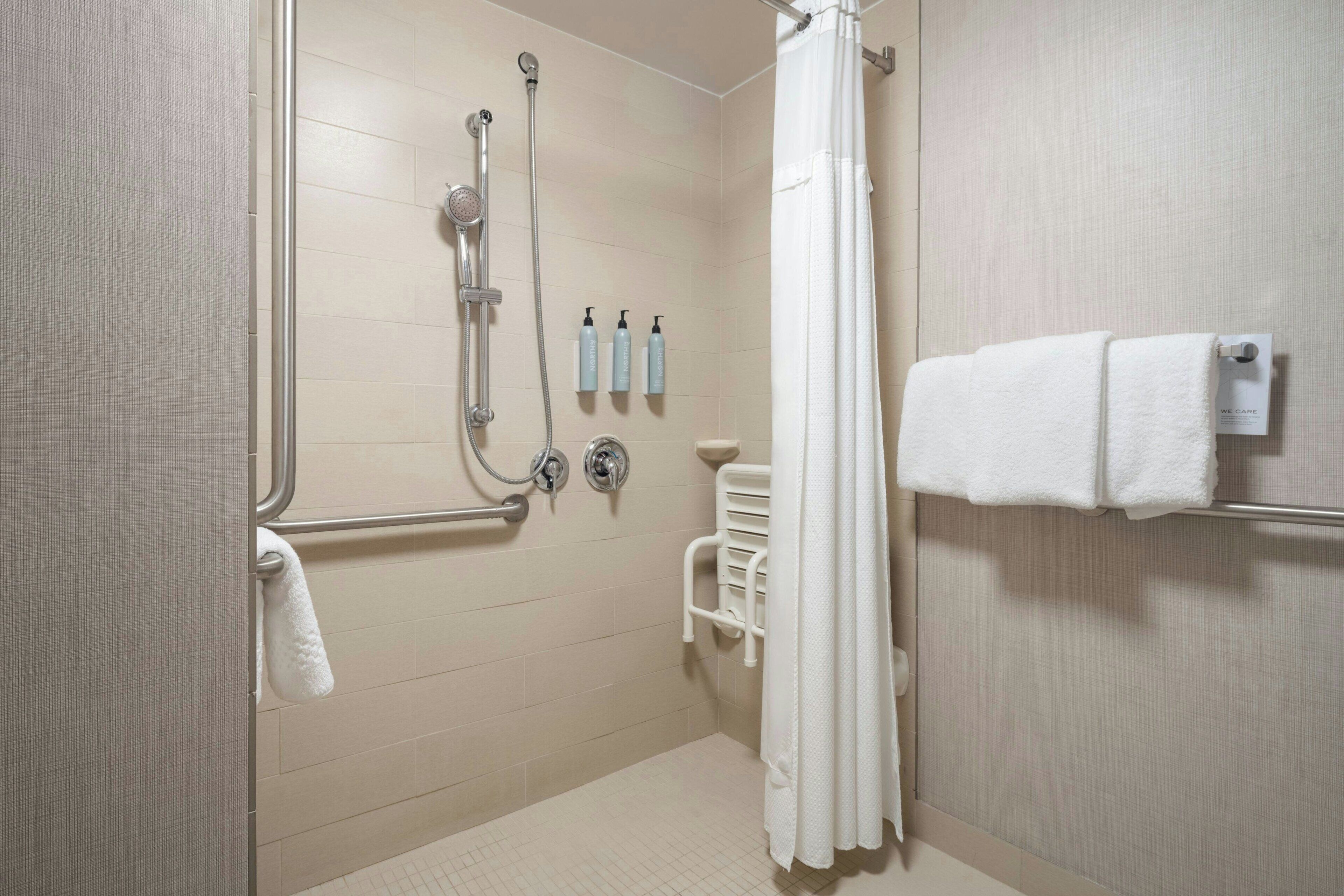 A shower area with a glass door, a handheld showerhead, a wall-mounted faucet, and a towel rack with two towels.