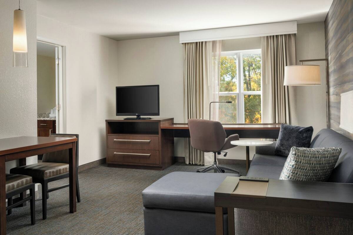 Habitación de hotel moderna con televisor de pantalla plana, sofá, mesa de comedor y escritorio pequeño.