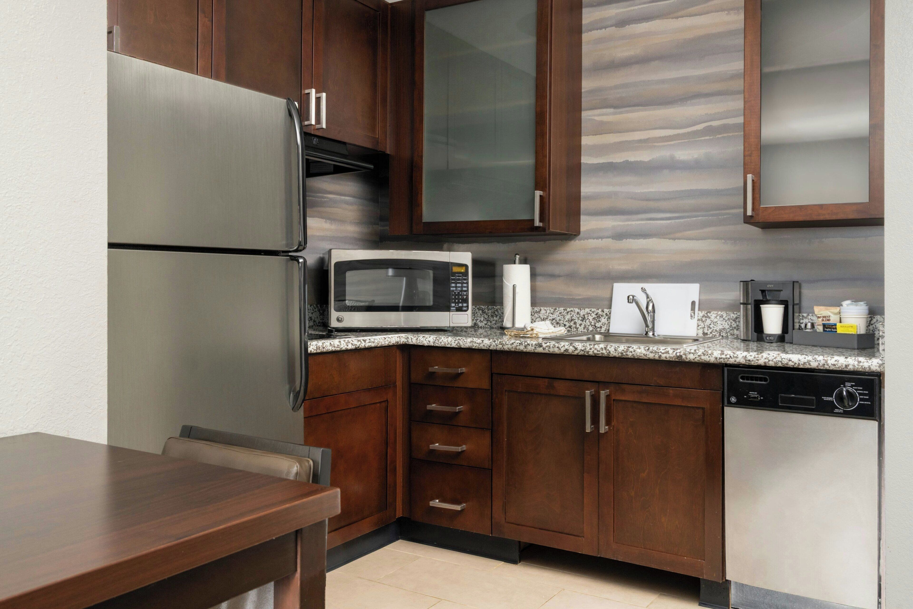 A kitchen with wooden cabinets, a stainless steel refrigerator, a microwave, a dishwasher, and a granite countertop.