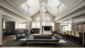 A spacious hotel lobby with a high ceiling, a fireplace, seating areas, and a large TV screen. - Residence Inn Springfield Chicopee (Chicopee)