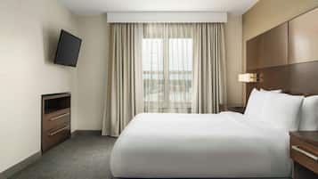 Habitación de hotel con una cama grande, un televisor montado en la pared, un escritorio con lámpara y una ventana con cortinas.
