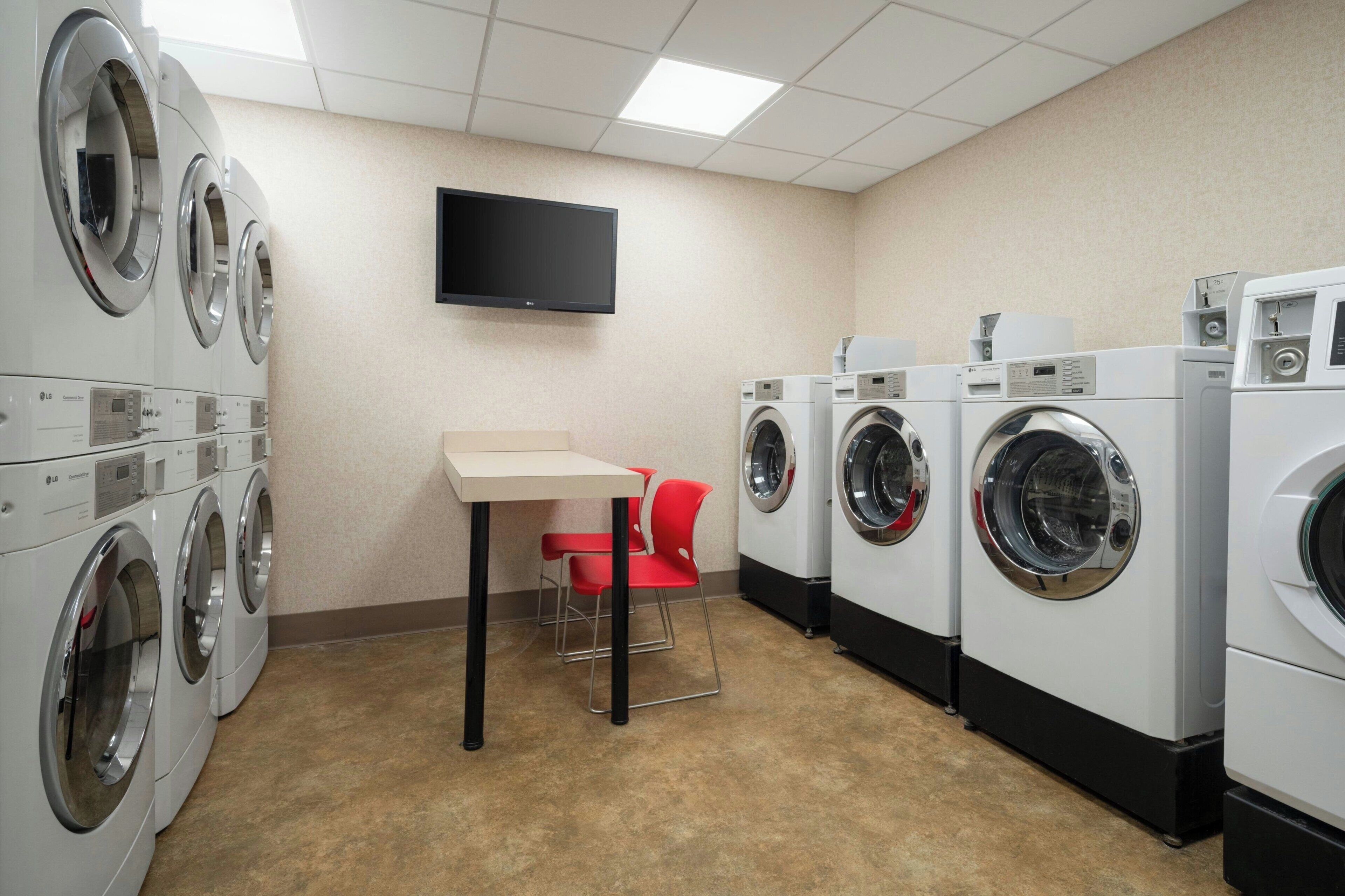 A laundry room with multiple washing machines, a table, and a chair.