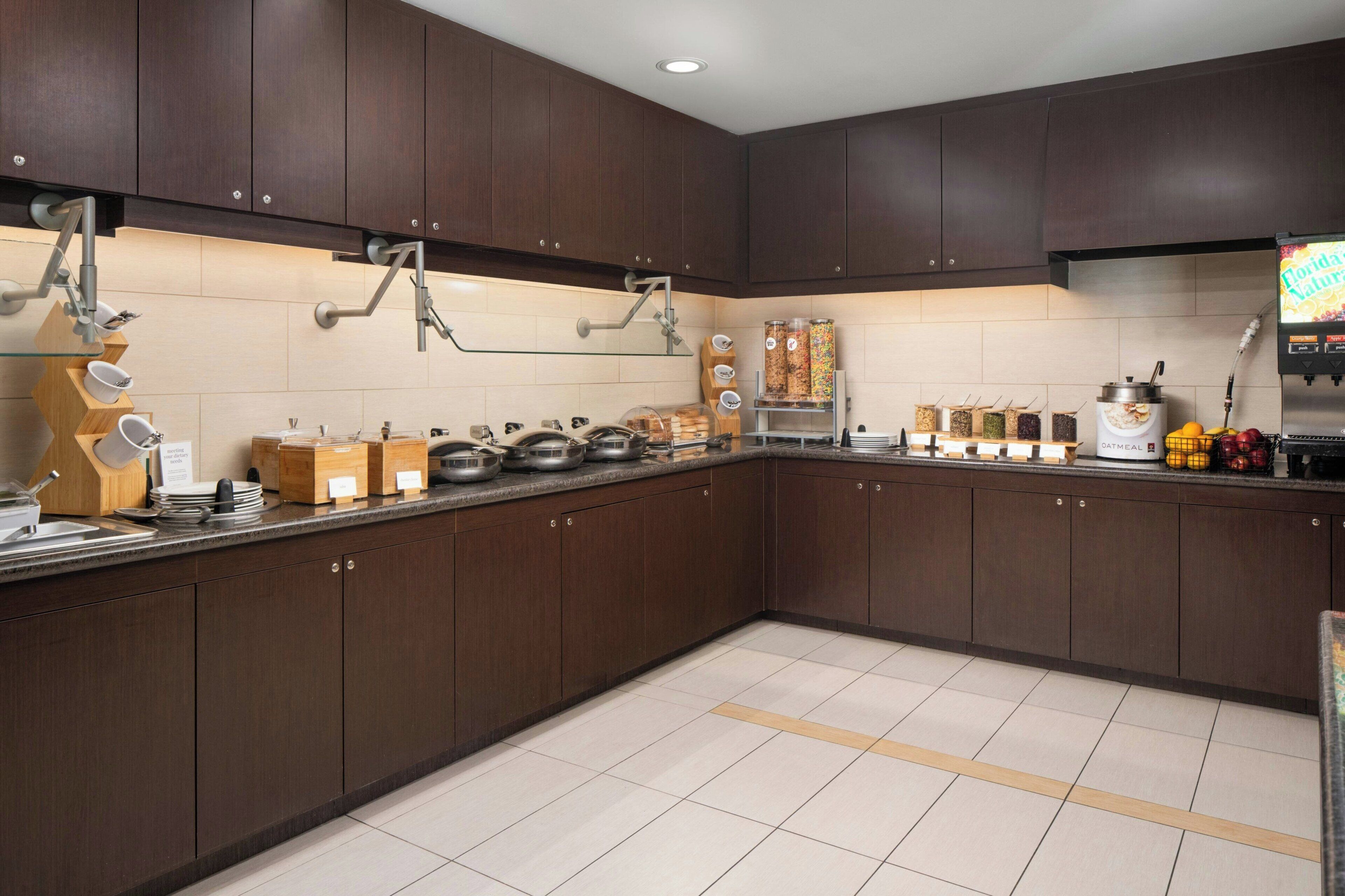 A modern kitchen with dark wooden cabinets, stainless steel appliances, and a variety of food items on the counter.