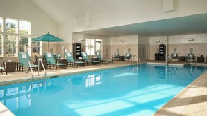 An indoor swimming pool with clear blue water, surrounded by lounge chairs and umbrellas. - Residence Inn Springfield Chicopee (Chicopee)
