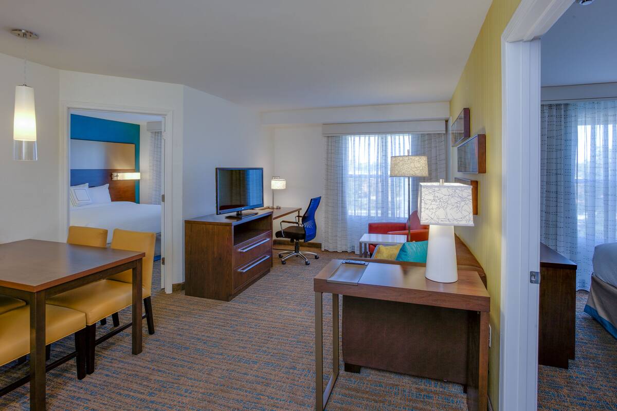 Habitación de hotel con cama, escritorio, silla, televisor y ventana con cortinas.