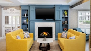 A modern living room with a fireplace, two yellow sofas, and a television above it.