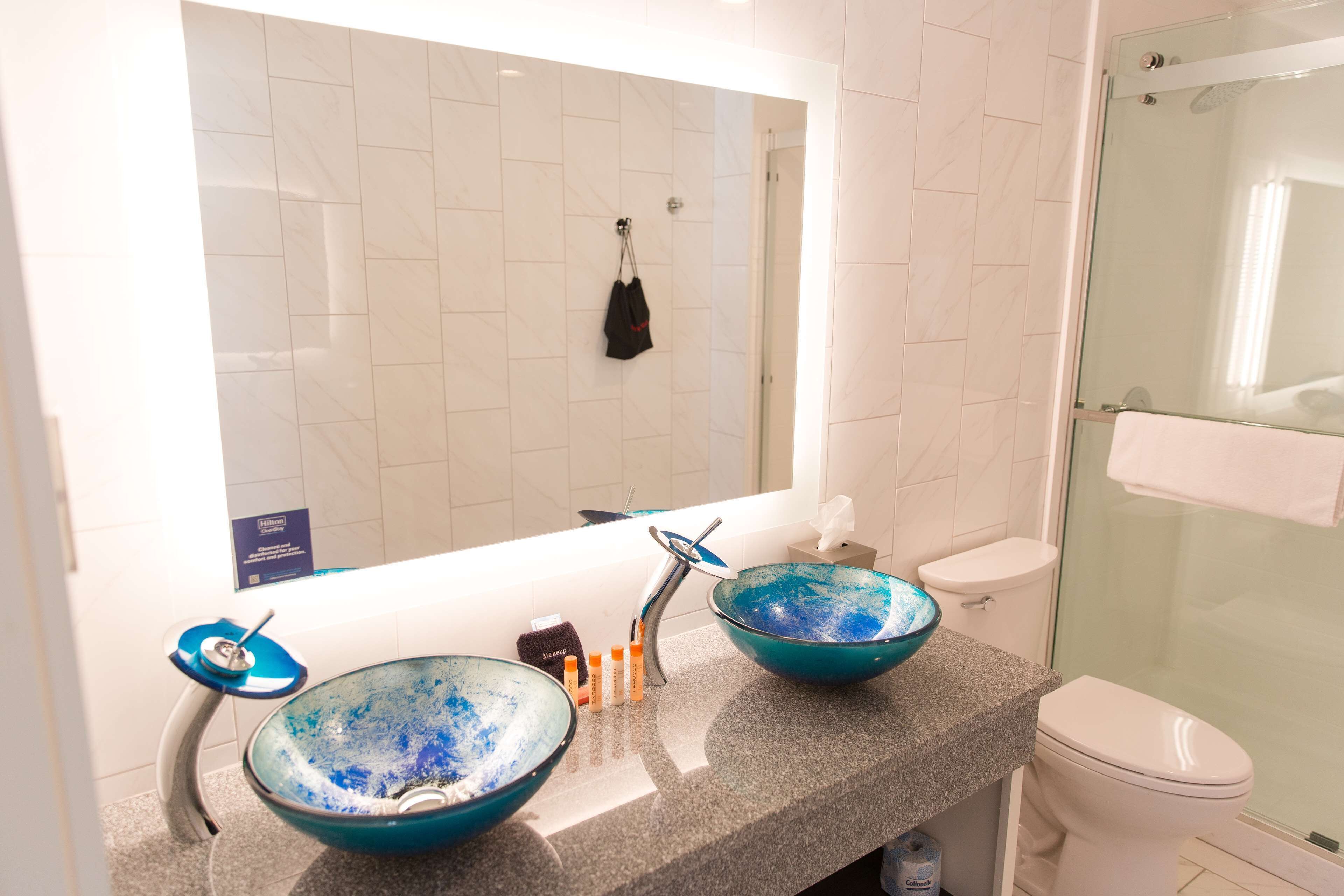 Une salle de bain avec deux bols en verre bleu posés sur le lavabo, des toilettes blanches et une douche en verre.