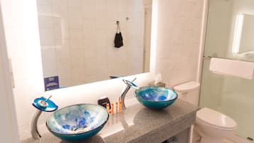 Une salle de bain avec deux bols en verre bleu posés sur le lavabo, des toilettes blanches et une douche en verre.
